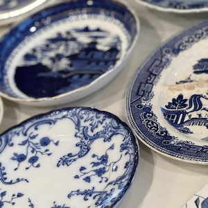 May include: A collection of antique blue and white porcelain plates and bowls. The plates feature various patterns, including floral designs and landscape scenes. The pieces are arranged on a light-colored surface, showcasing their intricate details and classic aesthetic.
