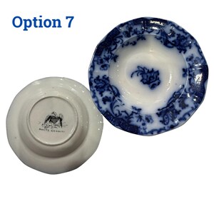 May include: Two antique white and blue ceramic plates. One plate is face up, displaying a blue floral pattern on a white background. The other plate is face down, revealing a black and white eagle emblem and the text "WHITE GRANITE".