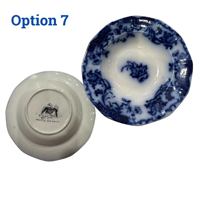 May include: Two antique white and blue ceramic plates. One plate is face up, displaying a blue floral pattern on a white background. The other plate is face down, revealing a black and white eagle emblem and the text "WHITE GRANITE".