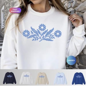 May include: White unisex sweatshirt featuring a light blue floral design across the chest. The design includes three flowers and leaves. The sweatshirt is shown with four other color options: navy, white, tan, and light blue.