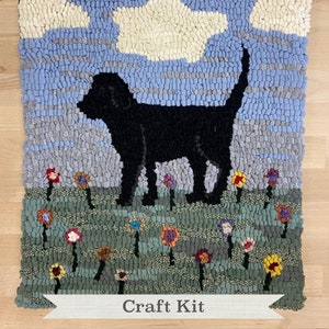 May include: A craft kit featuring a black dog standing in a field of flowers. The dog is silhouetted against a blue sky with white clouds. The kit includes all the materials needed to create a rug hooking project.