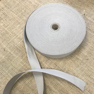 Puede incluir: Un rollo de cinta de algodón gris, un tipo de cinta de tela utilizada para coser, manualidades y otros proyectos.