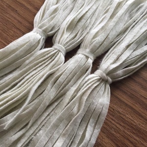 May include: Three bundles of white yarn with frayed ends, tied together at the top.