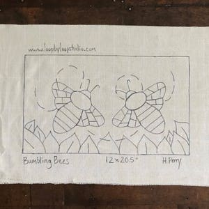 Puede incluir: Un dibujo en blanco y negro de dos abejorros en una tela de lino blanca con el texto "Bumbling Bees", "12 x 20.5"