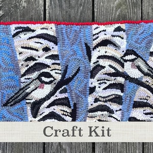 May include: Craft kit featuring a rug hooking pattern of blue and white birch trees with black branches and three small birds. The rug hooking pattern is framed with a red border. The text "Craft Kit" is printed on a banner below the rug hooking pattern.