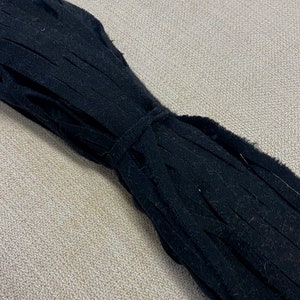 May include: A roll of black fringe trim, a type of fabric trim with long, thin strands hanging from a base fabric. The fringe is tightly rolled and tied together.