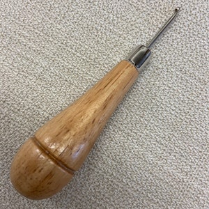 May include: A wooden crochet hook with a metal hook. The hook is about 6 inches long and has a rounded wooden handle.