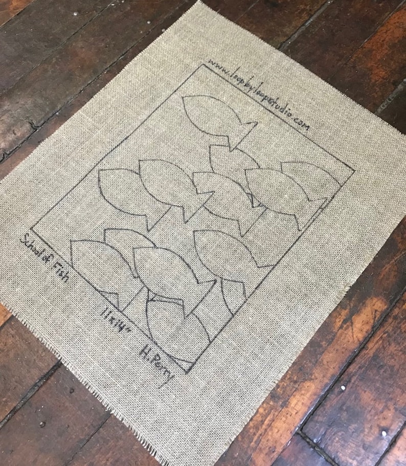 May include: A burlap fabric with a black outline of a school of fish. The text "School of Fish" and "11x14" H. Perry" is printed on the fabric.