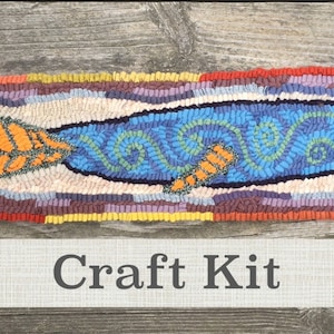 May include: A craft kit featuring a rug hooking pattern of a blue fish with orange fins and a colorful border. The kit includes all the materials needed to create the rug hooking project. "Craft Kit" is written on a banner below the image.