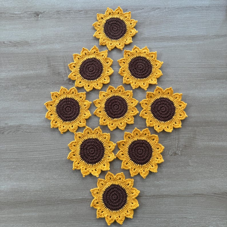 May include: A collection of ten handmade crochet sunflower coasters. Each coaster features a dark brown center and yellow petals, arranged in a diamond pattern on a wooden surface. The coasters are designed to protect surfaces from heat and moisture.