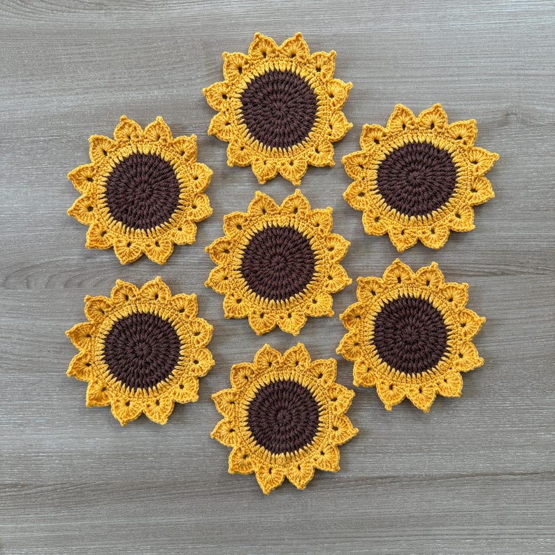 May include: Seven handmade crochet sunflower coasters. Each coaster features a brown center and yellow petals, resembling a sunflower. The coasters are arranged on a wooden surface, showcasing the intricate details of the crochet work.