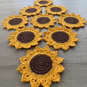 May include: A collection of handmade crochet sunflower coasters. Each coaster features a brown center and yellow petals, arranged in a sunflower design. The coasters are made of yarn and are suitable for placing drinks on.