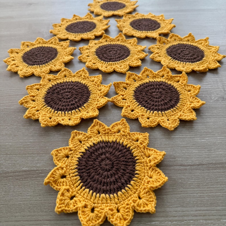 May include: A collection of handmade crochet sunflower coasters. Each coaster features a brown center and yellow petals, arranged in a sunflower design. The coasters are made of yarn and are suitable for placing drinks on.