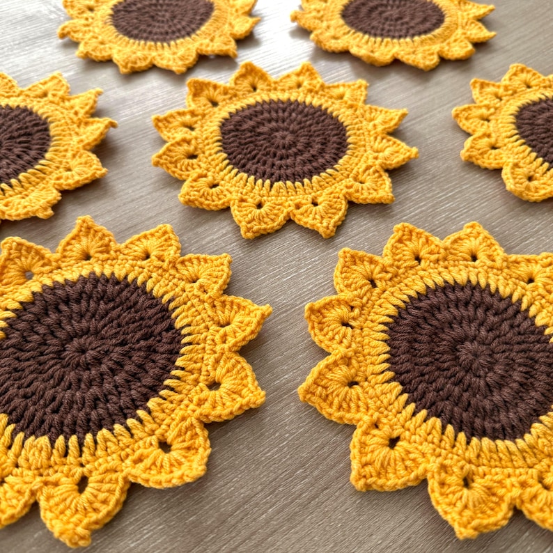 May include: Handmade crochet sunflower coasters. The coasters feature a brown center and yellow petals, resembling a sunflower. The coasters are made of yarn and are designed to protect surfaces from heat and moisture.