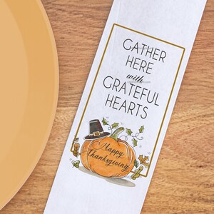May include: White paper napkin with a Thanksgiving design featuring a pumpkin with a pilgrim hat and the text "Gather Here with Grateful Hearts" and "Happy Thanksgiving".
