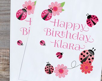 May include: Pink and white favor bags with a ladybug and flower design. The bags say "Happy Birthday Klara".