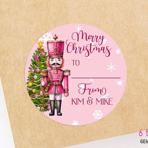 May include: Pink round Christmas gift tag with a pink and red nutcracker illustration, a Christmas tree, and the text "Merry Christmas to From Kim & Mike" with white snowflakes.