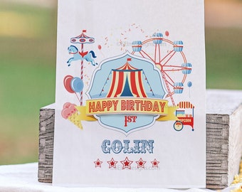 May include: White paper bag with a colorful circus-themed design. The bag features a Ferris wheel, a carousel, a tent, and a red ribbon with the text "Happy Birthday 1st Colin".
