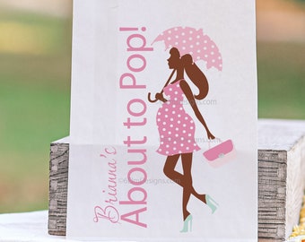 May include: White paper bag with a pink and white polka dot design. The bag has a silhouette of a pregnant woman holding an umbrella and a purse. The text on the bag reads "Briana's About to Pop!"
