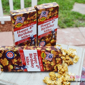 May include: Three popcorn boxes with a caramel corn design. The boxes have the text "Happy 4th Birthday Miles" and "October 10, 2017". The boxes also feature a Cubs logo and a cartoon image of a man with a dog.