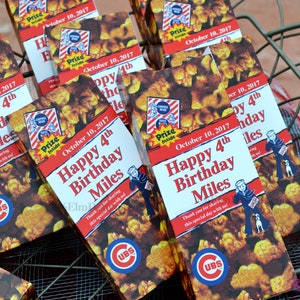 May include: A collection of popcorn boxes with a Cubs theme, featuring the text "Happy 4th Birthday Miles" and the date "October 10, 2017." The boxes are in a metal basket.