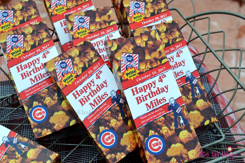 May include: A collection of popcorn boxes with a Cubs theme, featuring the text "Happy 4th Birthday Miles" and the date "October 10, 2017." The boxes are in a metal basket.