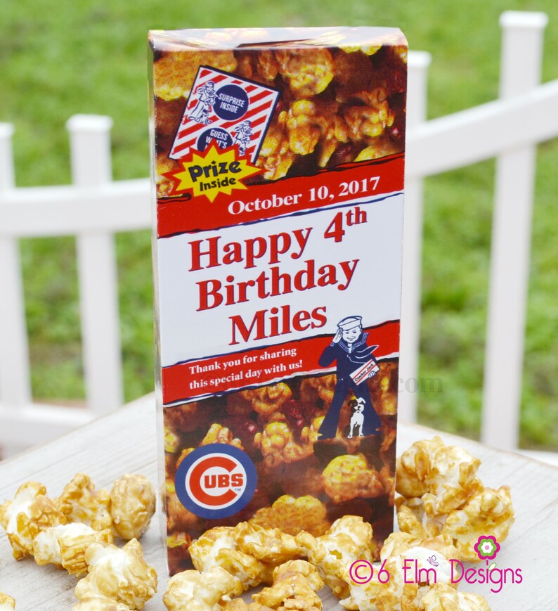 May include: A popcorn box with caramel popcorn and the text "Happy 4th Birthday Miles". The box has a red and white design with a sailor graphic and a "Prize Inside" logo. The Cubs logo is also visible.
