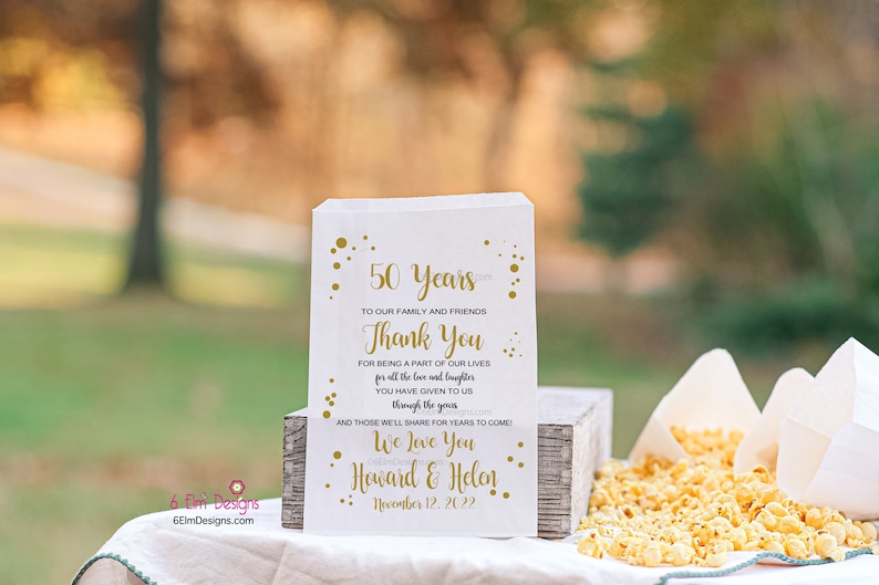May include: White favor bag with gold text and confetti. The text reads "50 Years To Our Family and Friends Thank You for being a part of our lives for all the love and laughter you have given to us through the years and those we'll share for years to come! We Love You Howard & Helen November 12, 2022".
