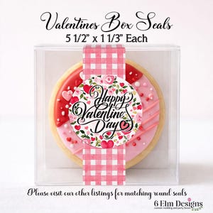 May include: A Valentine's Day cookie in a clear box, sealed with a pink and white gingham ribbon. The cookie is decorated with pink icing, red hearts, and the words "Happy Valentine's Day". The box seals are 5 1/2" x 1 1/3" each.