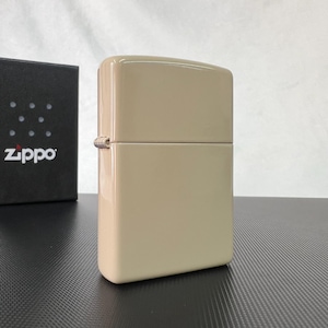 May include: A beige Zippo lighter with a glossy finish. The lighter is rectangular with rounded edges and a hinged lid. A black box with the Zippo logo is visible in the background.