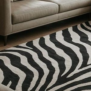 May include: A black and white zebra-striped rug is partially visible, placed on a wooden floor next to a gray sofa. The rug's pattern features bold, irregular stripes, creating a striking contrast. The sofa has a simple, modern design.