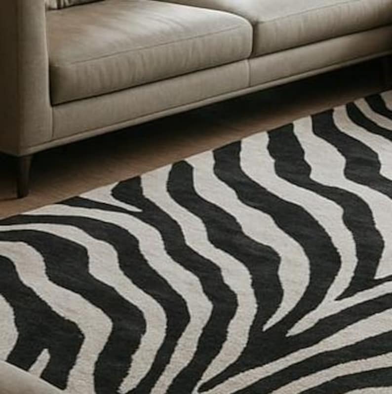 May include: A black and white zebra-striped rug is partially visible, placed on a wooden floor next to a gray sofa. The rug's pattern features bold, irregular stripes, creating a striking contrast. The sofa has a simple, modern design.