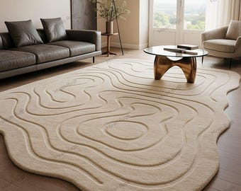 May include: Beige area rug with a topographic design. The rug features a series of raised, curved lines, creating a textured surface. The rug is placed in a living room setting, with a sofa, coffee table, and armchair.