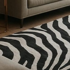 May include: A black and white zebra-striped area rug. The rug is rectangular and features a repeating pattern of black stripes on a light background. The rug is placed on a wooden floor, with a gray sofa visible in the background.