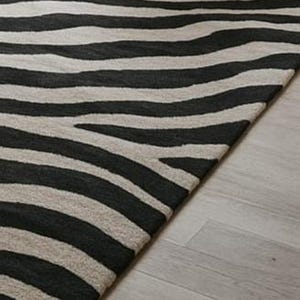 May include: A black and white striped rug with a zebra pattern. The rug is made of a soft material and has a textured surface. The rug is placed on a light-colored wooden floor.