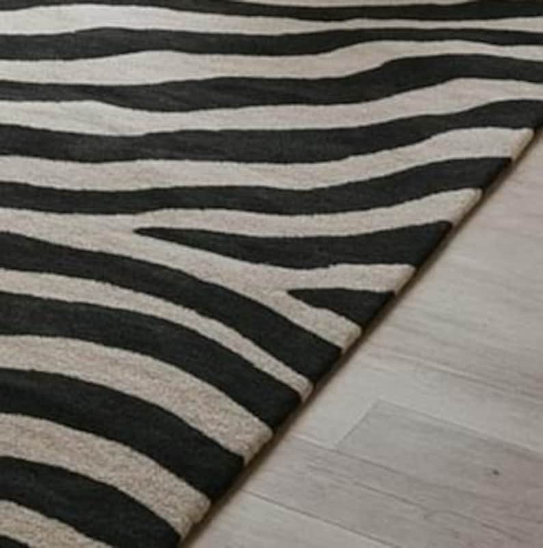 May include: A black and white striped rug with a zebra pattern. The rug is made of a soft material and has a textured surface. The rug is placed on a light-colored wooden floor.