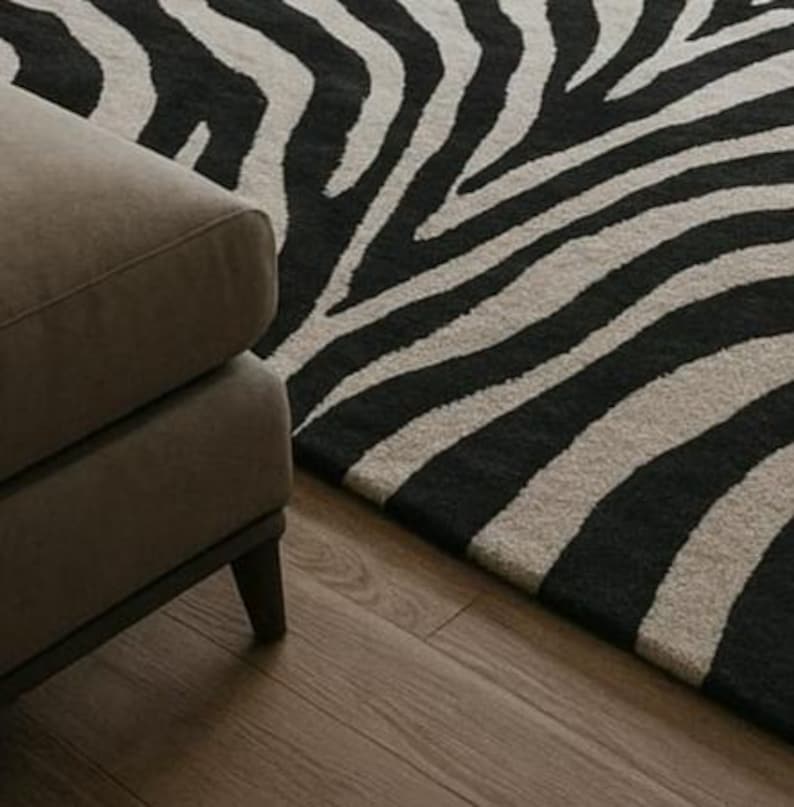 May include: A close-up of a zebra-striped rug in black and beige, with a section of a brown upholstered sofa in the foreground. The rug's pattern is bold and graphic, contrasting with the wooden floor.