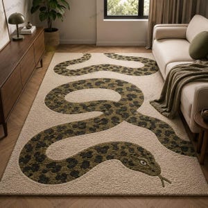 May include: A rectangular area rug featuring a large, winding snake motif with a dark olive green and black leopard-print pattern. The snake is set against a textured, light beige background, covering the majority of the floor space.