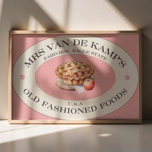 Könnte beinhalten: Ein gerahmter Druck mit einem Vintage-Design. Das Kunstwerk zeigt eine Aquarellillustration eines Apfelkuchens, eines Apfels und den Text "MRS VAN DE KAMP'S OLD FASHIONED FOODS U.S.A."