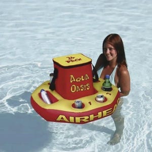 Puede incluir: Un enfriador flotante inflable rojo y amarillo con las palabras "Aqua Oasis" y "Airhead" impresas. El enfriador tiene una parte superior amarilla con las palabras "24 Pack" y contiene latas y una botella. El enfriador est&aacute; en una piscina.
