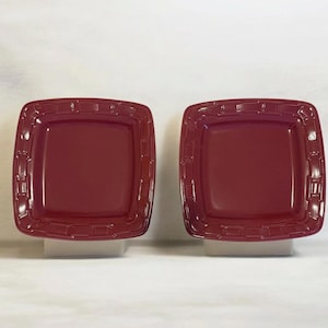 May include: Two square burgundy plates with a textured, woven-like border. The plates have a slightly raised rim and a smooth, flat center. The plates are displayed on a white surface against a white background.