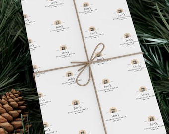 Könnte beinhalten: Ein verpacktes Geschenk mit weißem Papier mit einem sich wiederholenden Muster eines Bäckerei-Logos und dem Text "Jen's Sourdough Bread Bakery". Das Geschenk ist mit Bindfaden gebunden.