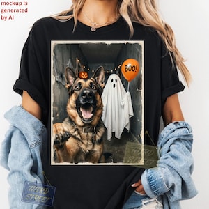 Puede incluir: Una camiseta negra de manga corta con un estampado gráfico de un perro pastor alemán con la boca abierta, una figura de fantasma blanca que sostiene un globo naranja con el texto BOO! y una pequeña calabaza en un pasillo oscuro.