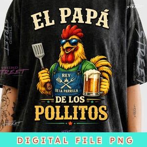 Peut inclure: Un t-shirt gris anthracite avec un motif de coq portant des lunettes de soleil et un tablier bleu. Le coq tient une spatule et une chope de bière. Le texte indique EL PAPA REY DE LA PARRILLA DE LOS POLLITOS. THIRD STREET est imprimé sur les manches.