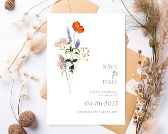 May include: A white 'Save the Date' card with watercolor floral illustrations. The card features an orange poppy, purple and blue flowers, and the text 'SAVE the DATE' with the wedding date 04.06.2027. The card is surrounded by dried flowers and a brown envelope.