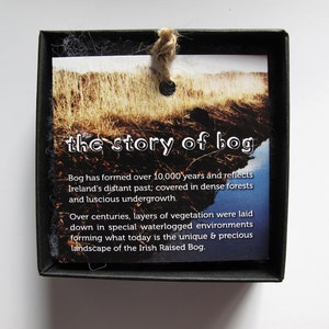 May include: A black box with a white card inside. The card has a picture of a bog and text that reads "the story of bog". The text on the card explains that bogs have formed over 10,000 years and reflect Ireland's distant past.
