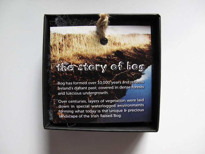 May include: A black box with a white card inside. The card has a picture of a bog and text that reads "the story of bog". The text on the card explains that bogs have formed over 10,000 years and reflect Ireland's distant past.