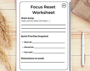 May include: A white Focus Reset Worksheet with black text, including sections for a brain dump, quick priorities, and distractions. A white pen and a small wrapped package are on a light wood surface.