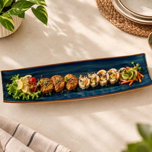 Puede incluir: Una fuente de servir rectangular y alargada de cerámica azul profundo con borde marrón, que contiene una variedad de rollos de sushi, aperitivos fritos, lechuga verde fresca, rodajas de limón, tomates cherry, pepino y zanahorias.