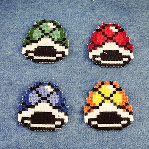 Peut inclure: Quatre patchs brodés représentant différents bonus de Super Mario Bros. Les patchs sont vert, rouge, bleu et jaune. Chaque patch a un contour blanc et des détails noirs.